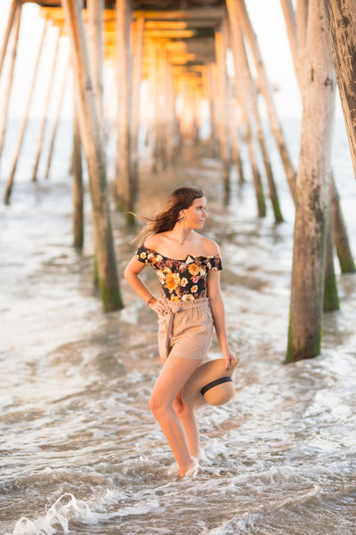 senior girl standing in water in the ocean under a boardwalk