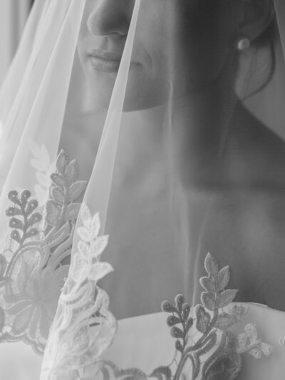 Black and white photo of bride's veil over her face and lacy dress