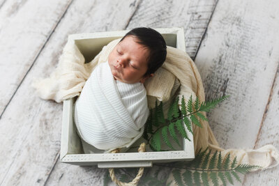 newborn baby wrapped in swaddling  white blanket laying in a wooden  box