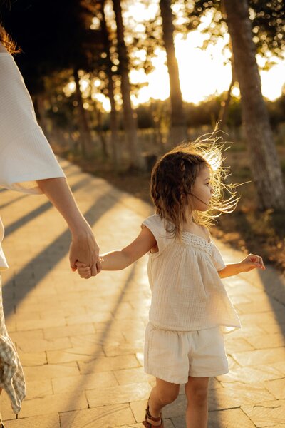 Adult hand holding child’s hand skipping on sunlit path | Rooted Within family connection