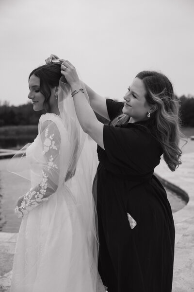 Blush Events wedding planner Jenny helping Wichita bride with bridal veil at outdoor Kansas wedding.