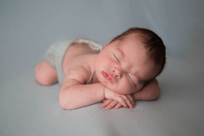 Newborn baby boy sleeping on his tummy while resting on his arms