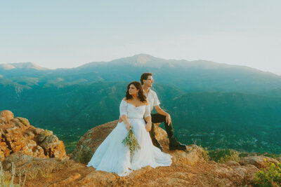 Bride and groom rest on rock during their Colorado elopement in front of Pikes Peak