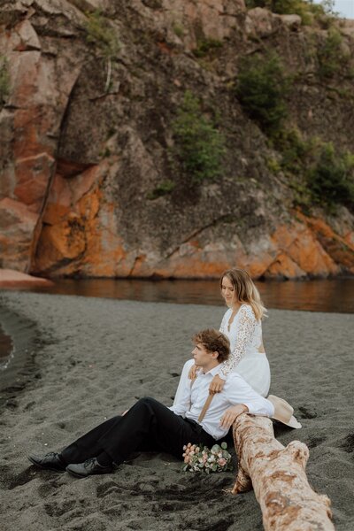 bride and groom sitting on a black beach