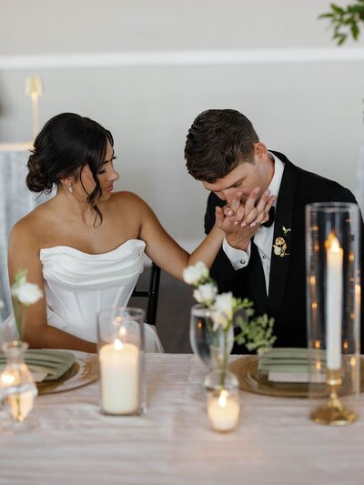 Groom gently kissing his bride’s hand during the reception, a quiet moment of tenderness and love.