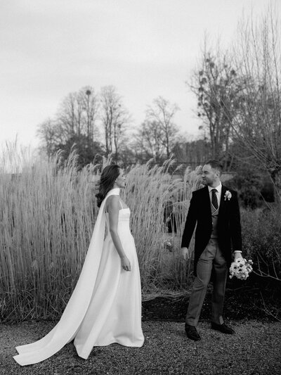 A bride and groom stopped in a field on their wedding day at Heckfield Place.