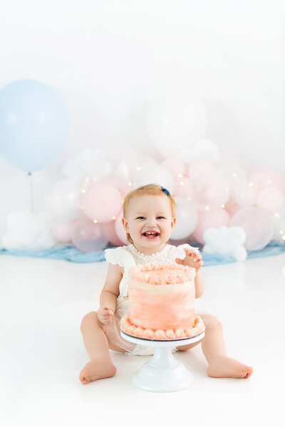 A toddler girl screams while smashing a cake in a pink dress