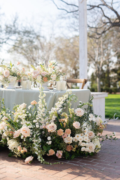 Close up of sweetheart table florals. Table cloth is pastel green and florals are a mix of pink, peach, cream, and greenery