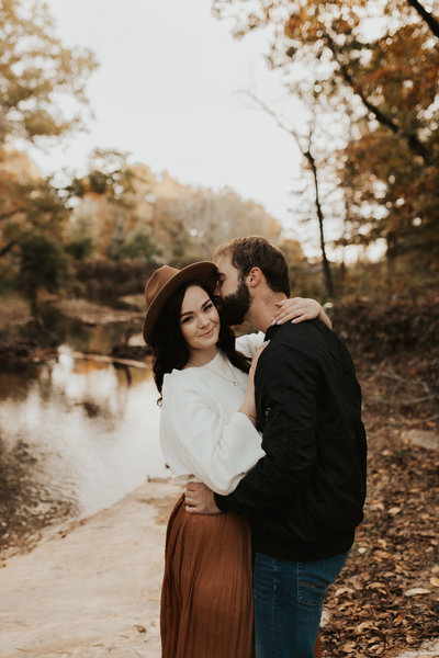 couple standing and holding each other by a creek of water