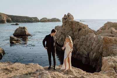 bride and groom walking on rocks in the ocean