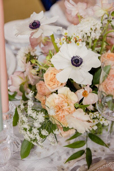 elegant floral arrangement with white anemones, peach roses, and lush greenery in a refined tablescape setting