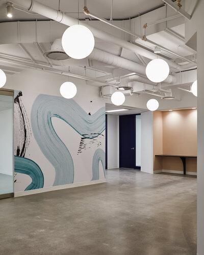 A spacious reception area featuring a bold, abstract, black and blue wall mural, and bright, modern globe pendant lights