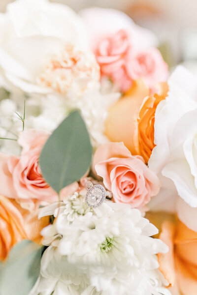 flowers for the bride with pastel orange and pink flowers and a silver oval engagement ring