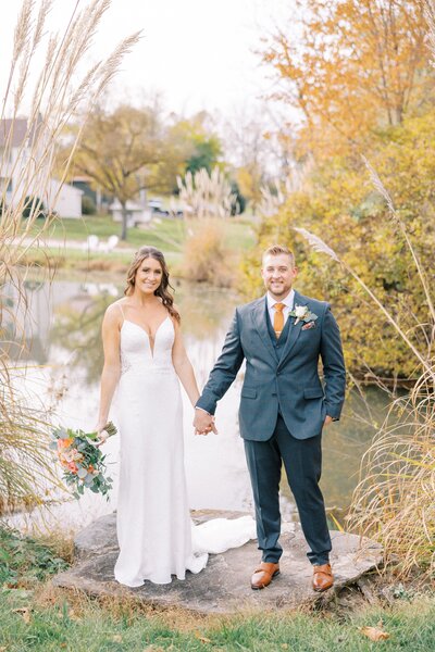 Bride and groom pose in front of pond with autumn colors