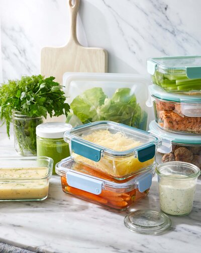 Healthy, fresh food stored in glass storage containers. Leafy greens, carrots and soups are visible.