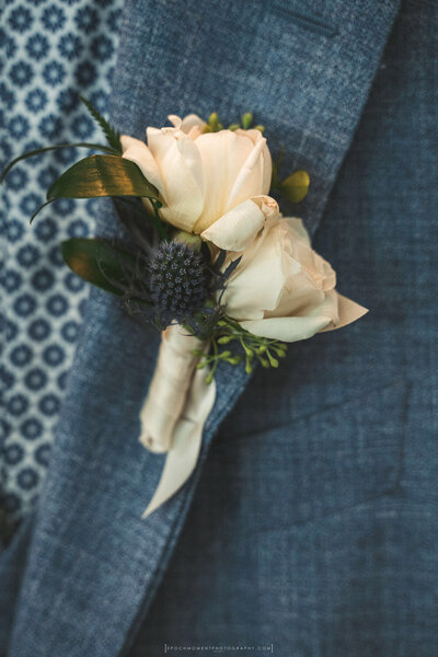 Groom boutonniere with cream rose and thistle on blue suit jacket