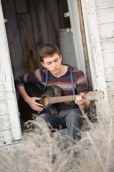 Senior boy playing his guitar in a field in Boise, ID.