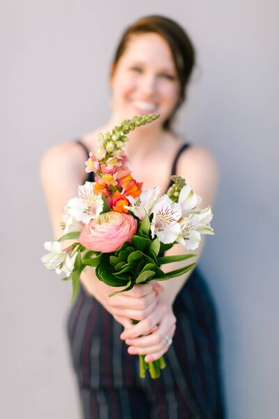 Caitlyn Gray holding a bouquet of flowers by a gray wall.