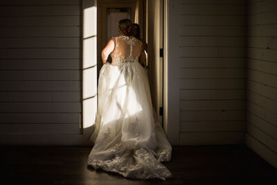 Bride walking toward a doorway with sunlight casting shadows.