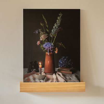 Een stilleven met in het midden een bloemstuk in okerkleurige aardenwerken vaas met rondom persoonlijke voorwerpen zoals een verrekijker, boeken en trouwringen.