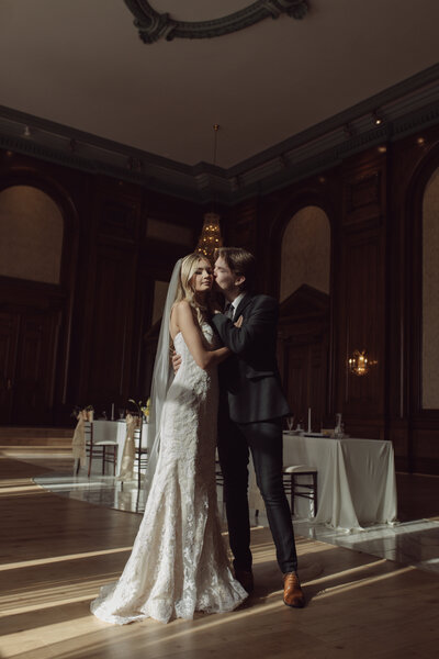 Vintage and dark wedding inspired couple kisses bride on the cheek at the Madison venue in Utah.