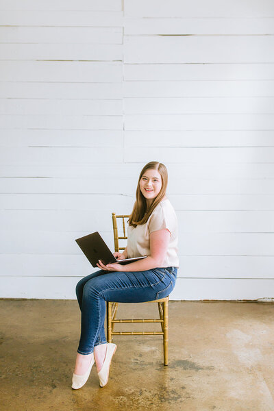 luxury photographer sitting in a gold chair with her macbook pro in her lap