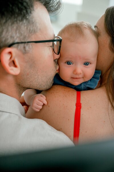 in studio father kissing baby who is being held by her mother 