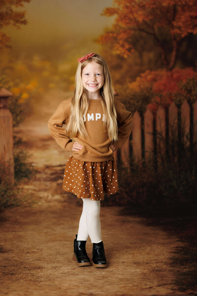 little girl in a pumpkin sweatshirt, skirt, and tights on a warm autumn backdrop 