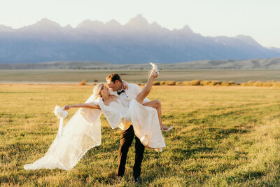 photo of groom holding bride in a field with mountains in the background taken by Jackson Hole elopement photographer