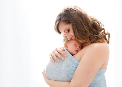 a mother and her baby boy wrapped in blue in front of a bright window