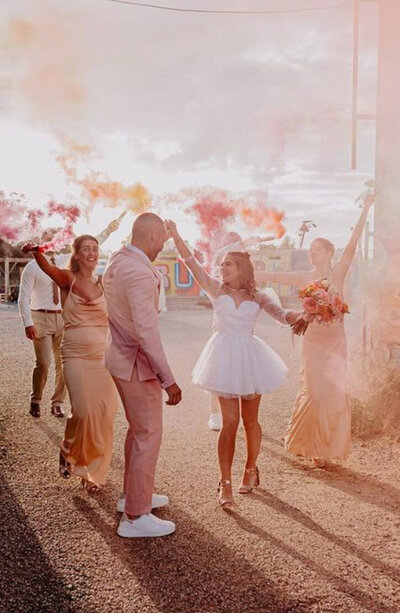 Jeunes mariés faisant joyeusement la fête avec leurs invités, brandissant des fumigènes colorés en extérieur et immortalisés par Laura, photographe en vendée.