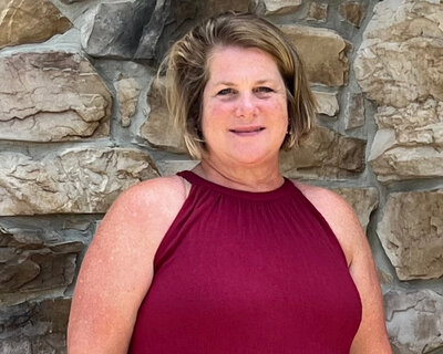 Sue Leardi posing for a headshot behind a rustic stone wall. 