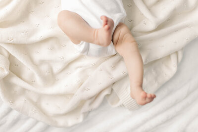 Close-up of newborn baby’s legs resting on a soft, cream knit blanket during an in-home Kansas City newborn session