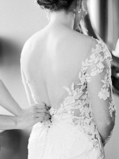 Black and white image of hands zipping up the back of a bride's wedding dress