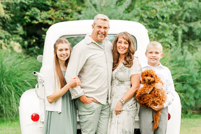 Family standing by a white, vintage truck together outdoors.