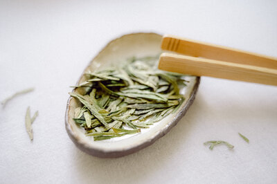 Tea leaves on a table with a tea cup in the background