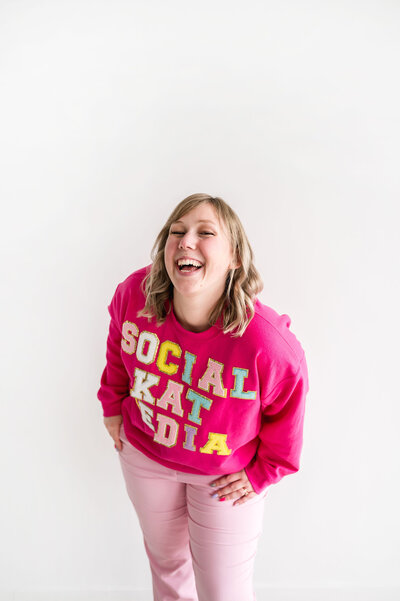 Kat Murphy in a pink Social Kat Media sweatshirt in front of a white wall