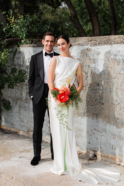 Groom driving convertible car while bride sits on the back wearing sunglasses
