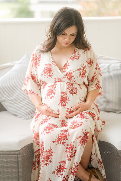 A brunette pregnant woman in a floral gown gazes down at her bump.
