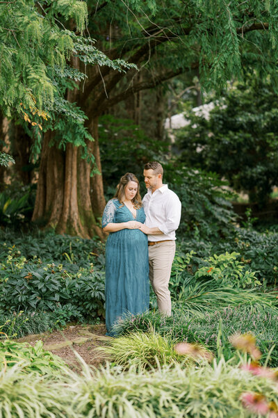 Dad and pregnant mom hold belly during maternity photos at Raleigh Rose Garden