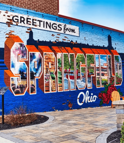 Colorful Springfield, Ohio mural reading 'Greetings from Springfield' in vibrant street art style, reflecting the vibrant community that Black Bear Roofing & Exteriors proudly serve with expert roofing & exterior services.
