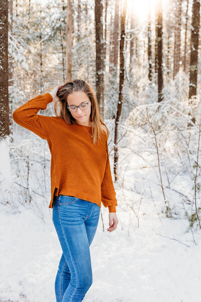 high school girl in an orange sweater playing with hair in the snow