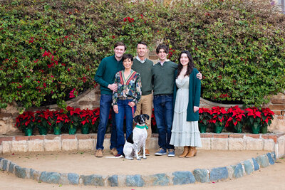 A family of five with a white and black dog standing against greenery at the Mission San Juan Capistrano