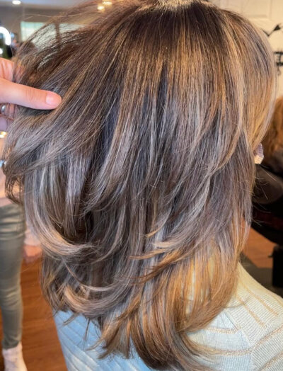 A close-up view from the back of wavy, healthy-looking hair with expertly done blonde highlights and darker lowlights, showcasing dimension and shine.