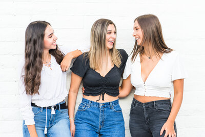 Three senior girls laughing in front of white wall