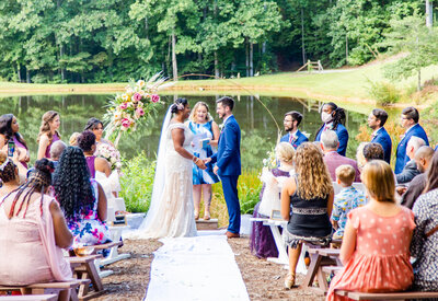 bride and groom holding hands at wedding ceremony in front of a pond