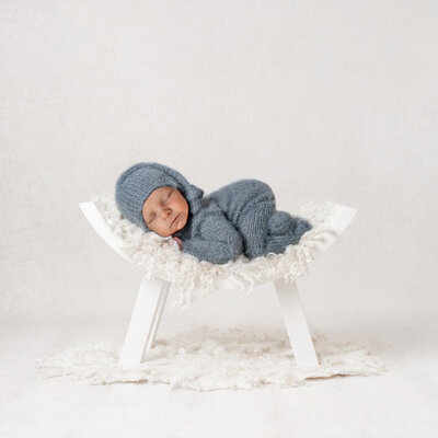 baby boy in blue sleeps on a white bench with butt up in the air