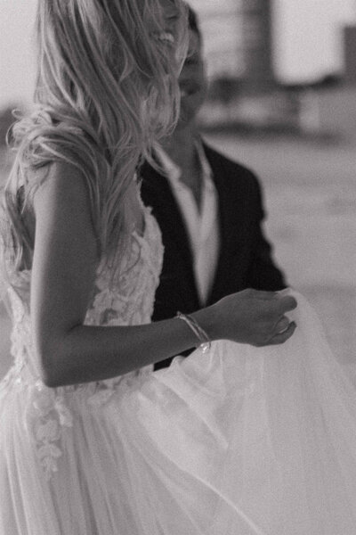 Beach bride twirls in gauzy dress in the foreground while her husband looks on with smile on his face