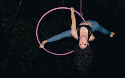 Aerialist Andrea Mason posing on Lyra with a gorgeous smile, with a purple aerial hoop.