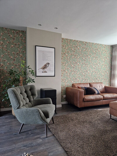 Interieur met groene muur met bloesemprint, vintage fauteuil en cognackleurige bank